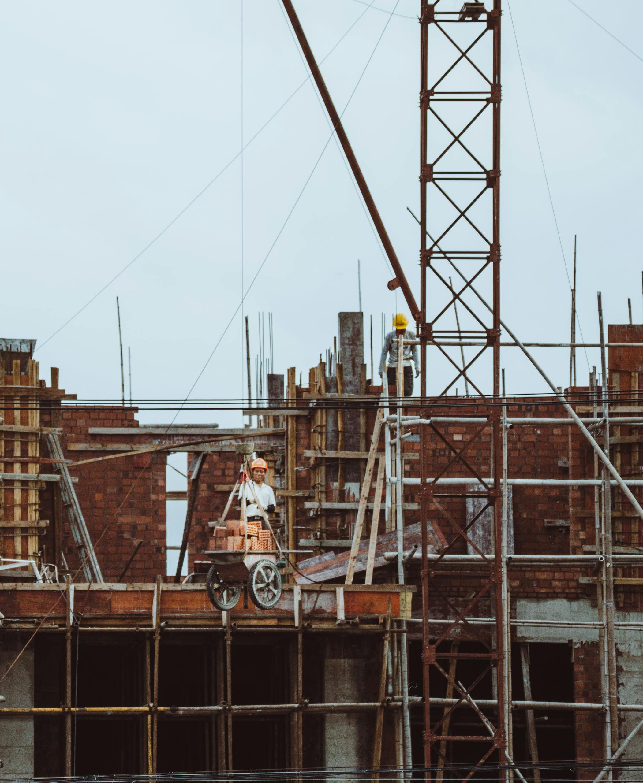 A construction worker on a scaffold at a building site with cranes and brickwork visible.